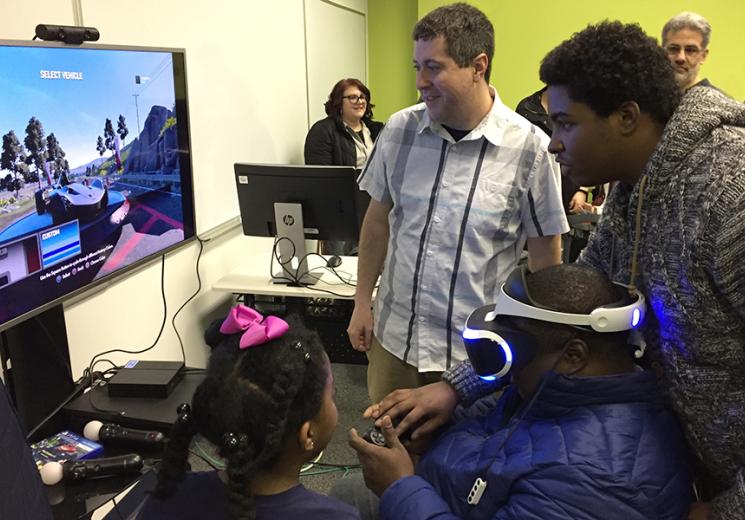 Ryan Lizardi looks on as a prospective student and his family try out a virtual reality game in the IMGD lab